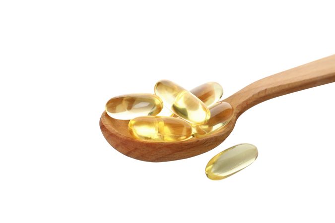 Wooden spoon with omega pills, isolated on blank background