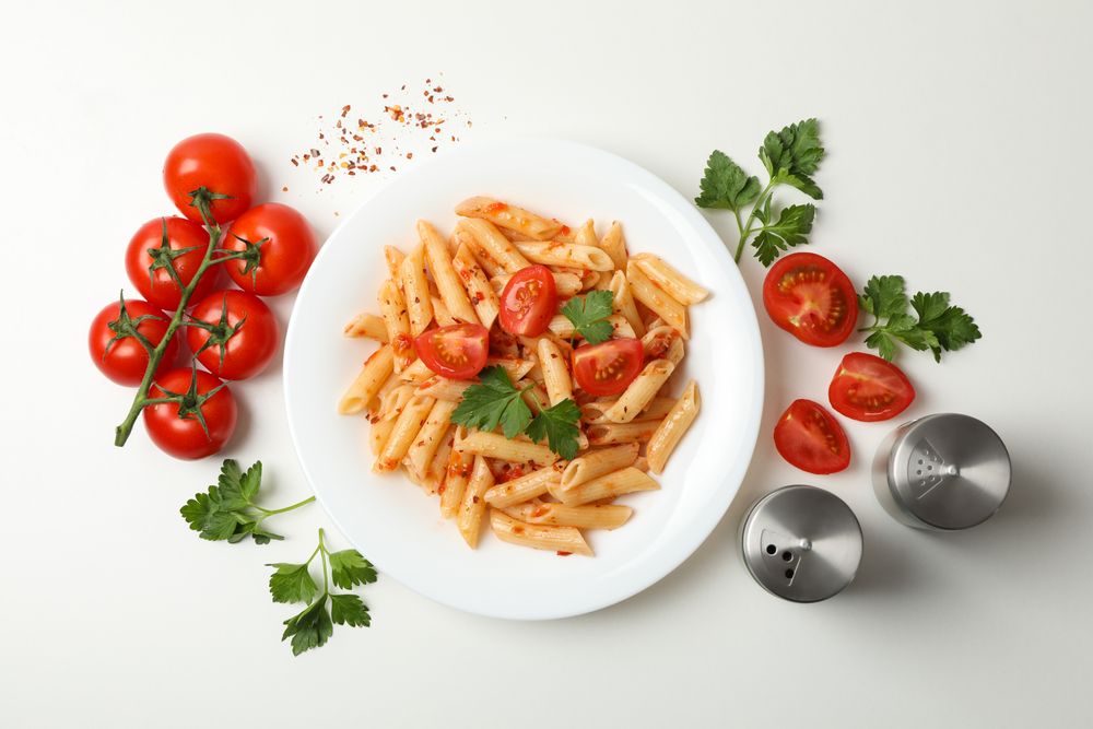 Composition with plate of tasty pasta and ingredients for cooking on plain background