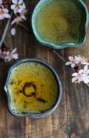 Top view of Asian style green tea set and blooming peach tree branch on wooden table