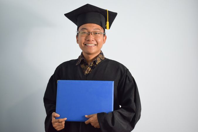 Happy and proud male graduate in studio shoot holding certificate