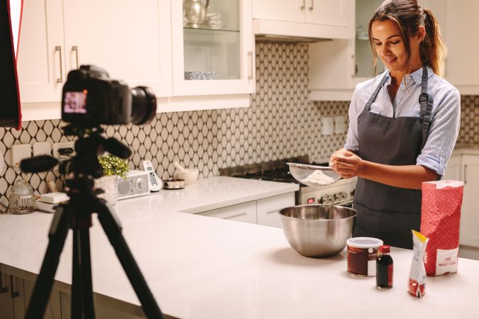 Video camera filming young female blogger in kitchen