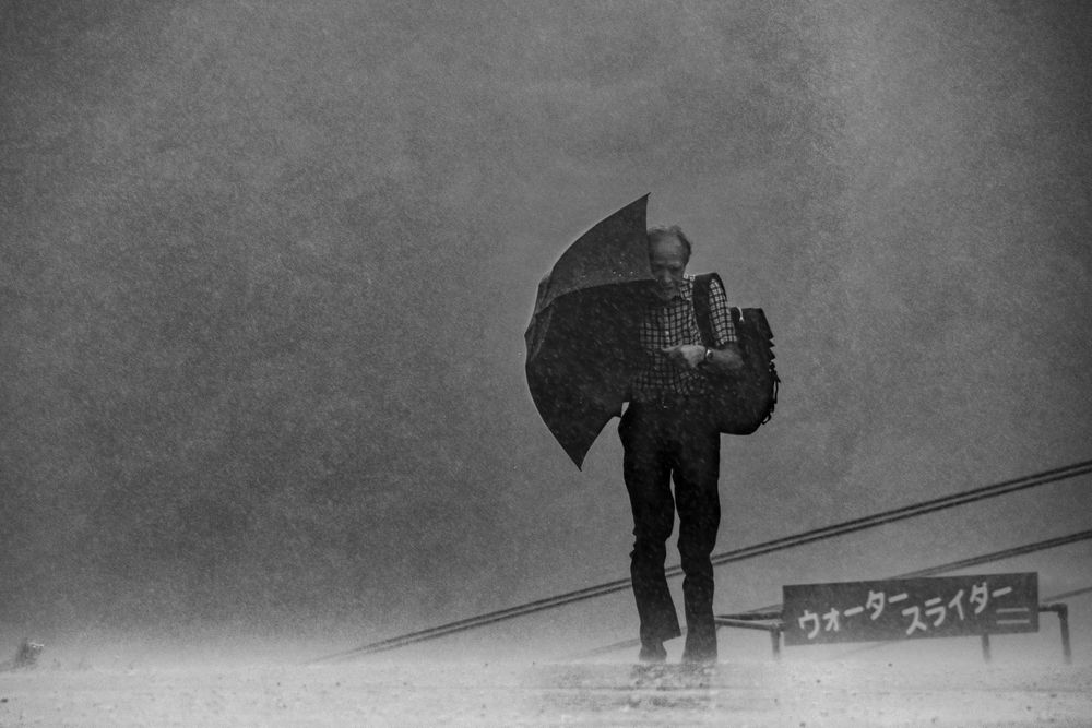 Grayscale photo of an older man holding an umbrella on a rainy day