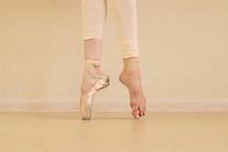 Ballet dancer’s feet, one in pointe shoes during practice.
