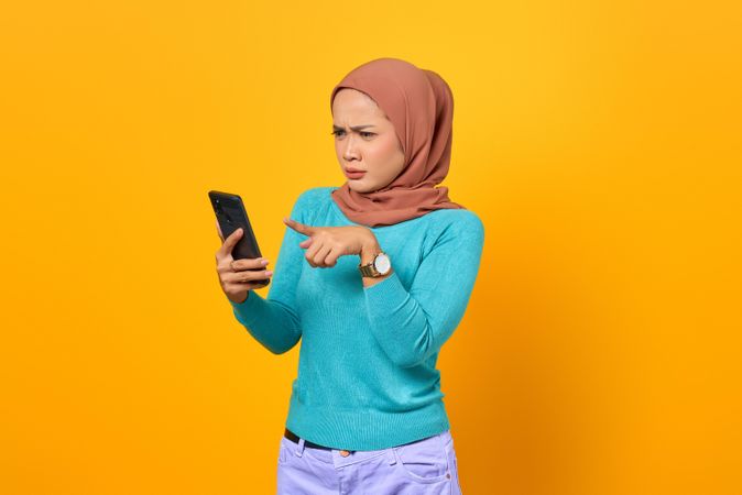 Confused Muslim woman pointing at her smart phone