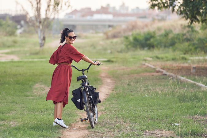 Cheerful young woman traversing park with bicycle