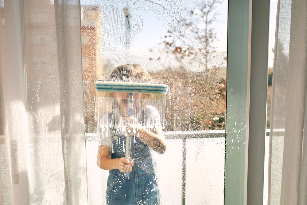 Unrecognizable boy washing windows at home