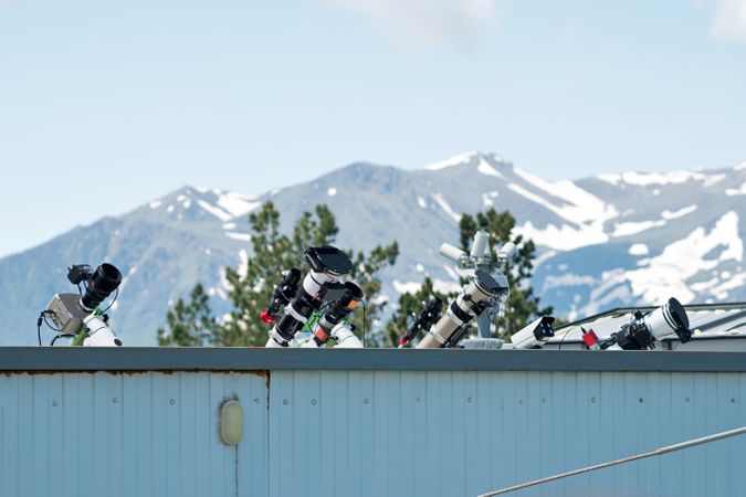 Telescopes on rooftop with mountains in background.