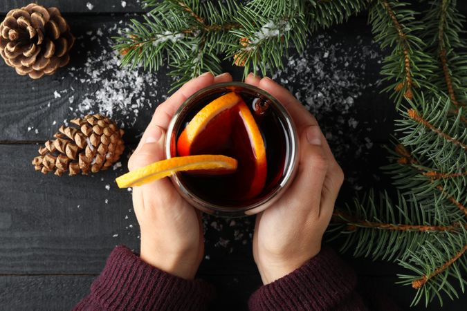 Girl holding glass with mulled wine on decorated wooden background, top view