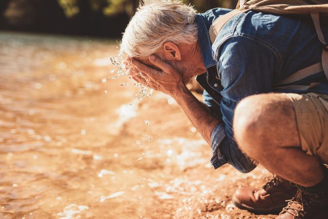 Side portrait of a mature man washing his face in the lake during a hike