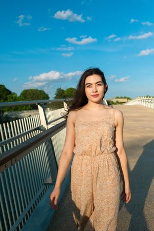 Peaceful woman in dress walking along rural bridge