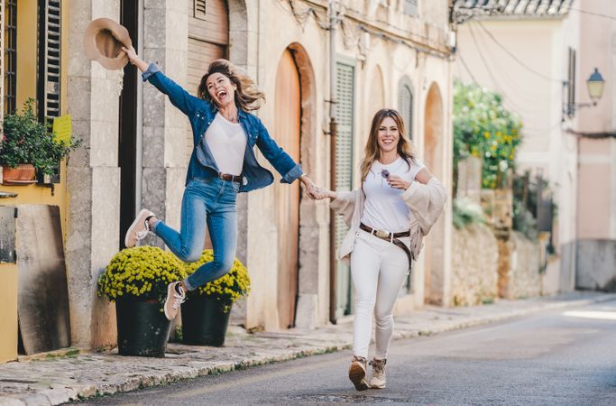 Friends having fun and jumping holding hands in street