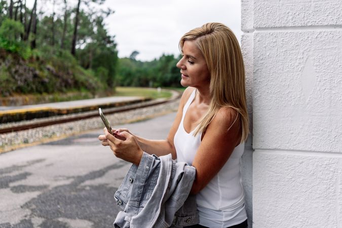 Contented woman staying on railway station with smartphone