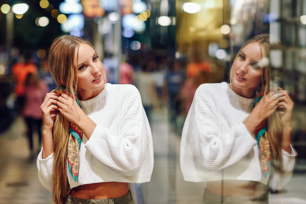 Woman fixing long hair in window reflection