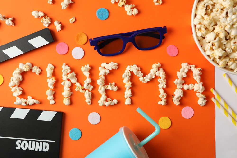 Word cinema laid out from popcorn and movie watch accessories on orange background