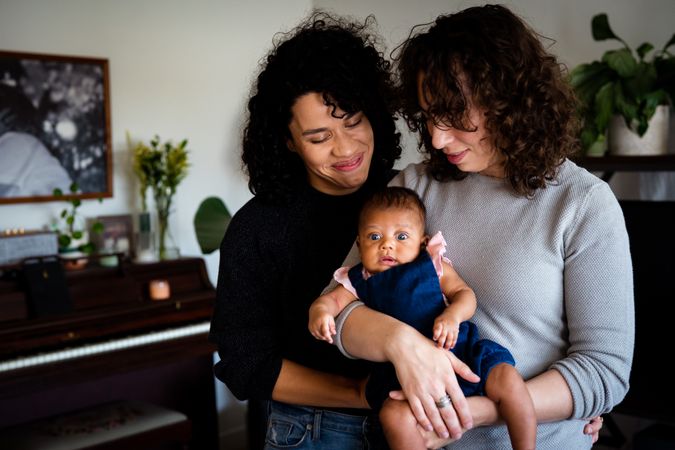 Two new mothers holding and looking down on their newborn baby girl