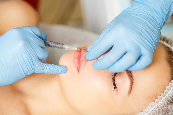Hands in latex gloves injecting beauty treatment into mouth