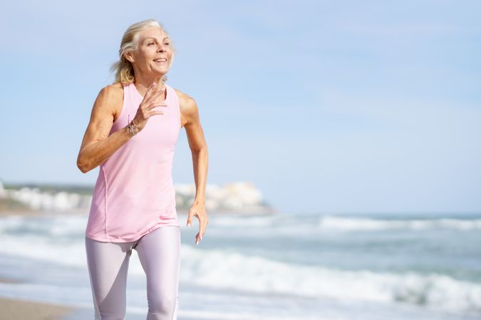 Healthy older woman in sports gear jogging along beach