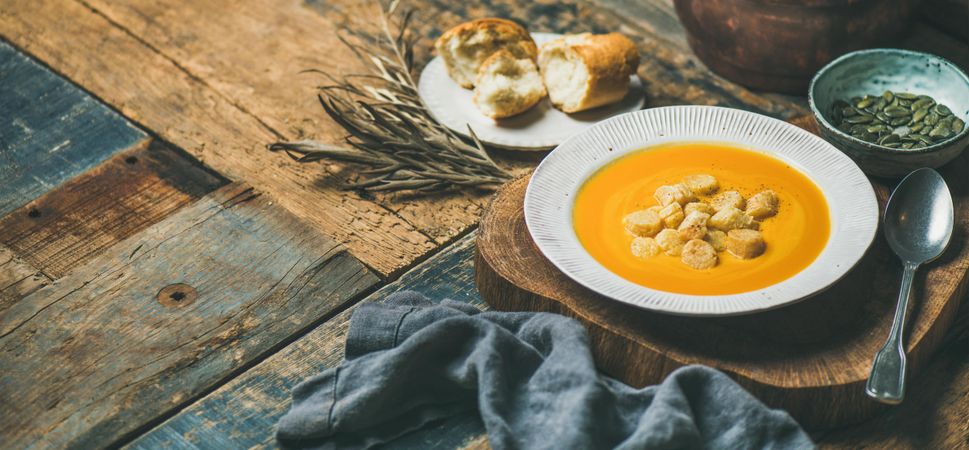 Pumpkin soup with croutons, seeds, spoon and bread on wooden table