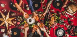 Group of people toasting with drinks at festive red table with cake, roast chicken, and decorations