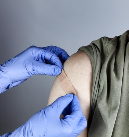 Vaccine shot being bandaged by hands in latex gloves