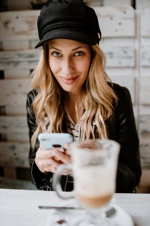 Smiling curly woman browsing smartphone at table