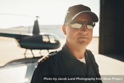 Pilot in cap and sunglasses inside hangar with helicopter in background 4A7R60