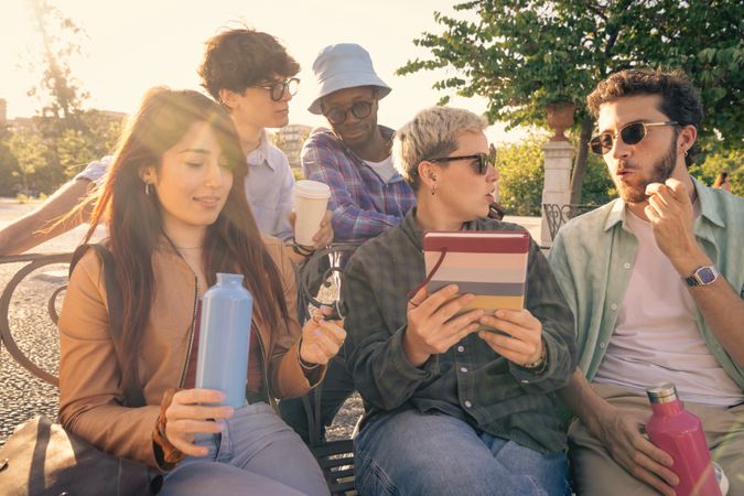 Diverse group of students collaborating with a laptop outdoors on a park bench.