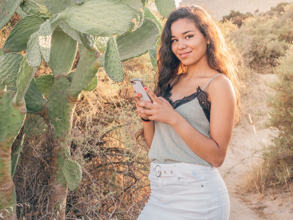 Playful trendy young woman texting at deserted countryside
