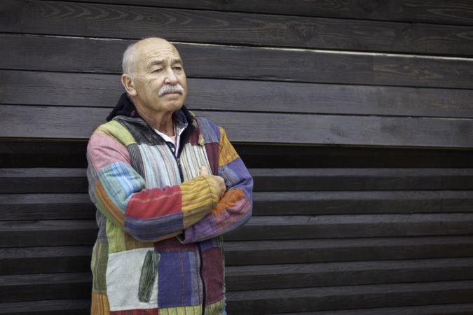 Pensive older man with arms folded against house
