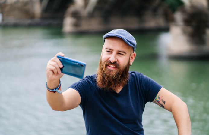 Satisfied male tourist taking selfie on smartphone at quay