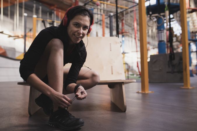Smiling woman with headphones lacing shoe in gym