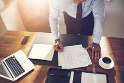 Overhead shot of man in business attire writing on paper at his desk