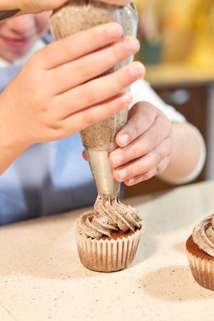 Crop girl decorating cupcakes with pastry bag