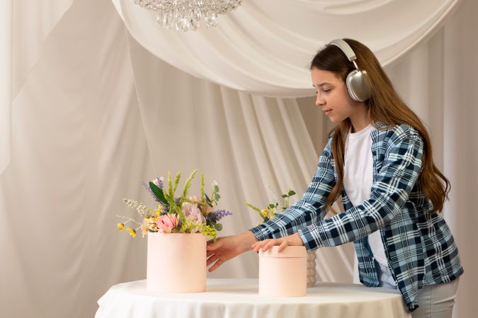 Girl arranging flower bouquets on a table wearing headphones.