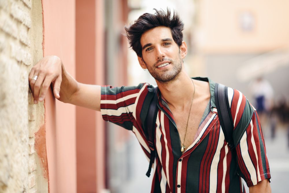 Confident man with dark hair wearing casual clothes leaning on wall outdoors