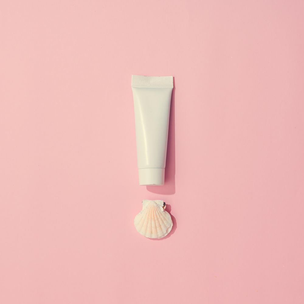 Sunscreen and shell on pastel pink background