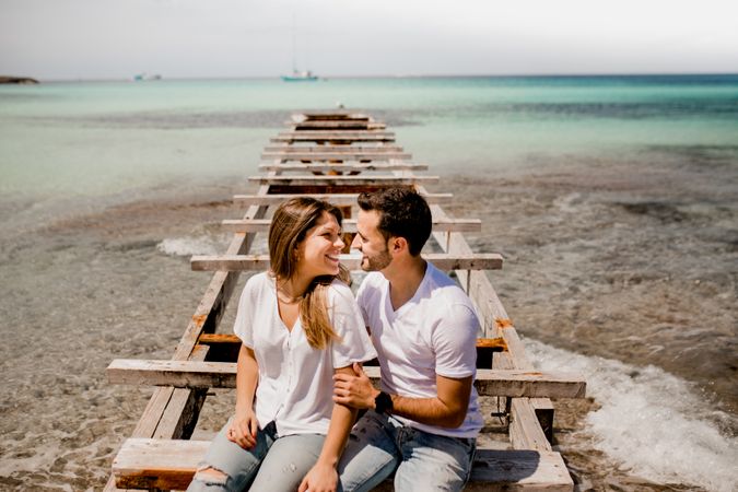 Glad lovers sitting on destroyed pier on seashore