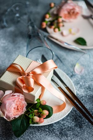 Pink flowers next to gift with pink ribbon on grey table