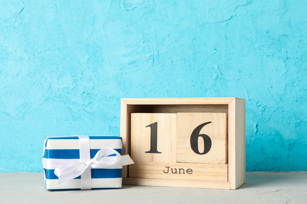 Wooden cubes calendar date June 16 and gift box on table against color background, space for text