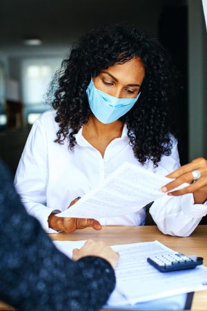 Woman with colleague going through documents at a work meeting while wearing a facemask