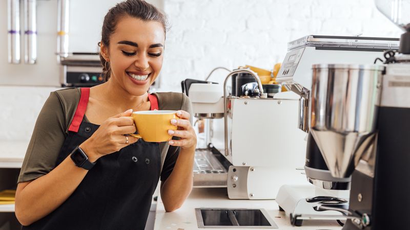 Beautiful cheerful barista holding a mug and looking at camera