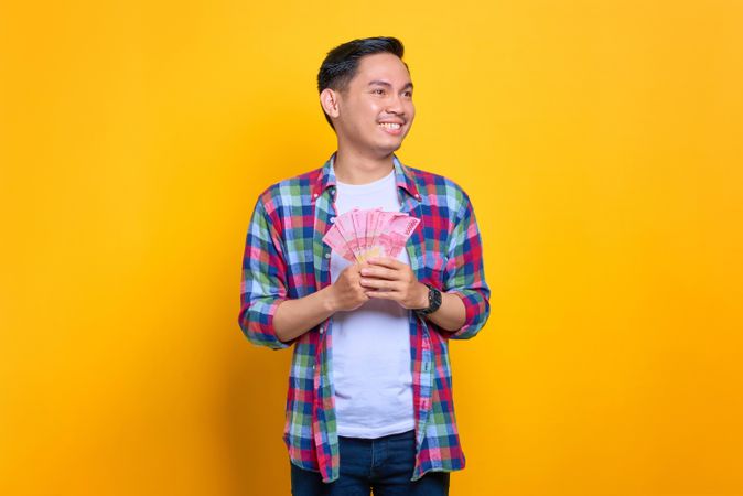 Very happy Asian man holding winning money in studio shoot