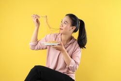 Happy Asian Young Woman Eating Fried Instant Noodles using Fork