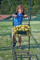 Smiling boy pushing cart with balls for padel