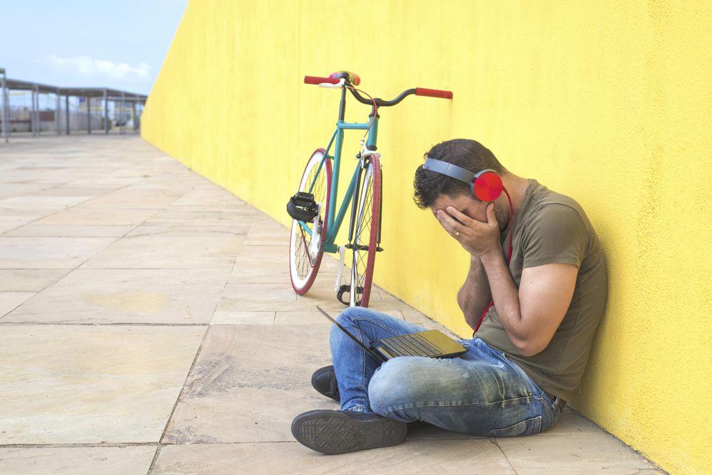 Stressed male with red headphones sitting outside concentrating on laptop