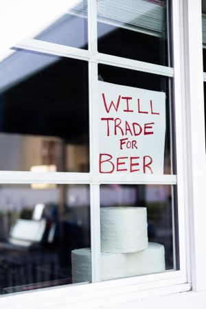 Angled view of handmade sign in home window asking to trade toilet paper for beer
