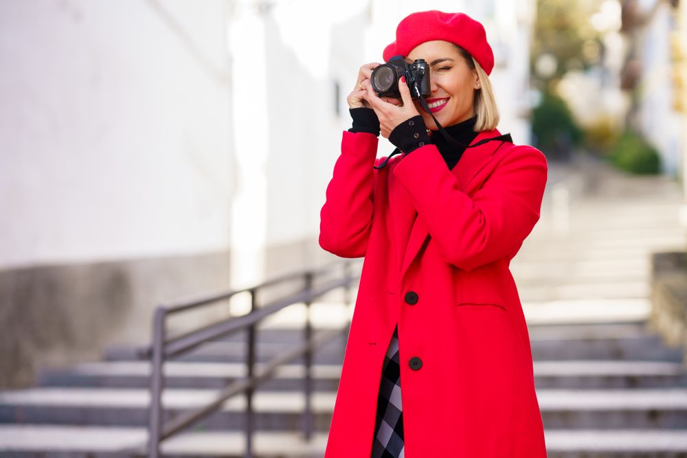 Female photographer in stylish clothes taking photo while standing on stairs in city