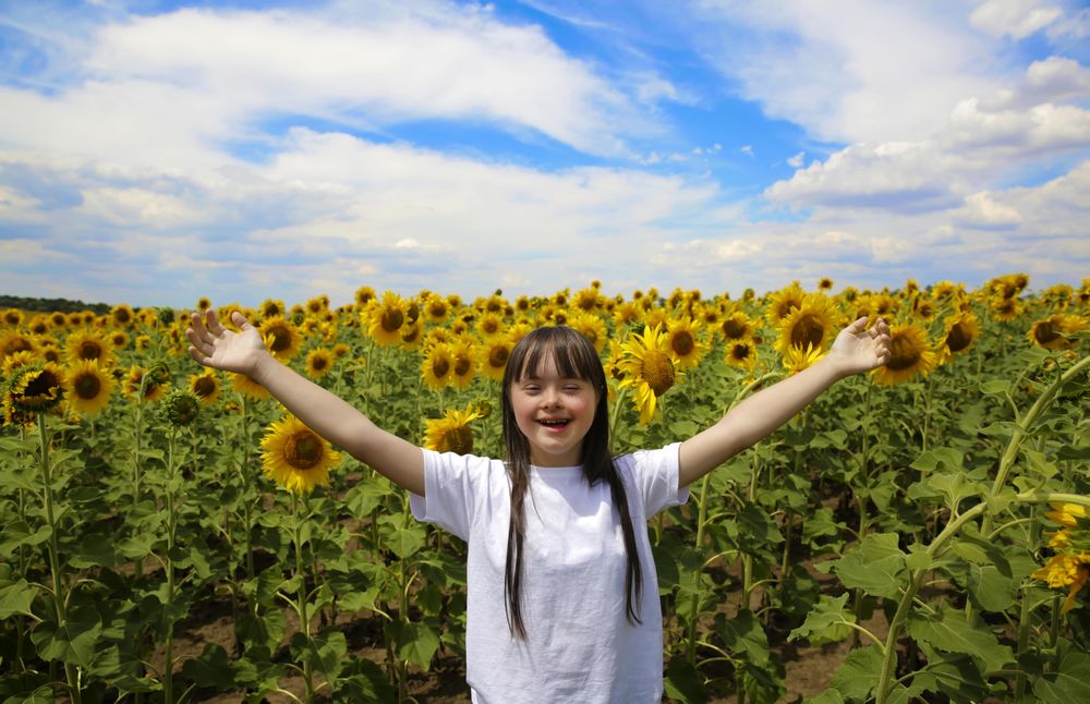 Excited young girl with Down syndrome standing in a flower field