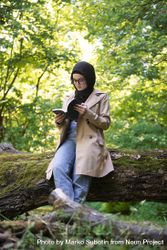 Middle Eastern woman sitting on mossy tree with book 5raAM0