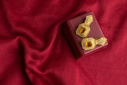Beautiful shiny golden earrings with diamond studded Indian traditional design on a red velvet background